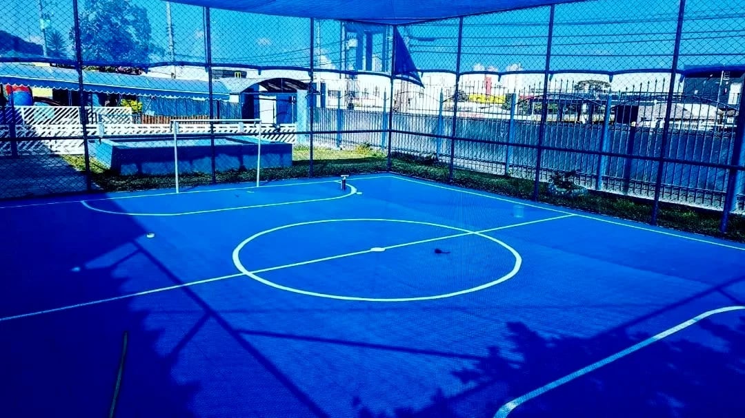 Quadra azul com cobertura de tela, marcações brancas e alambrado.