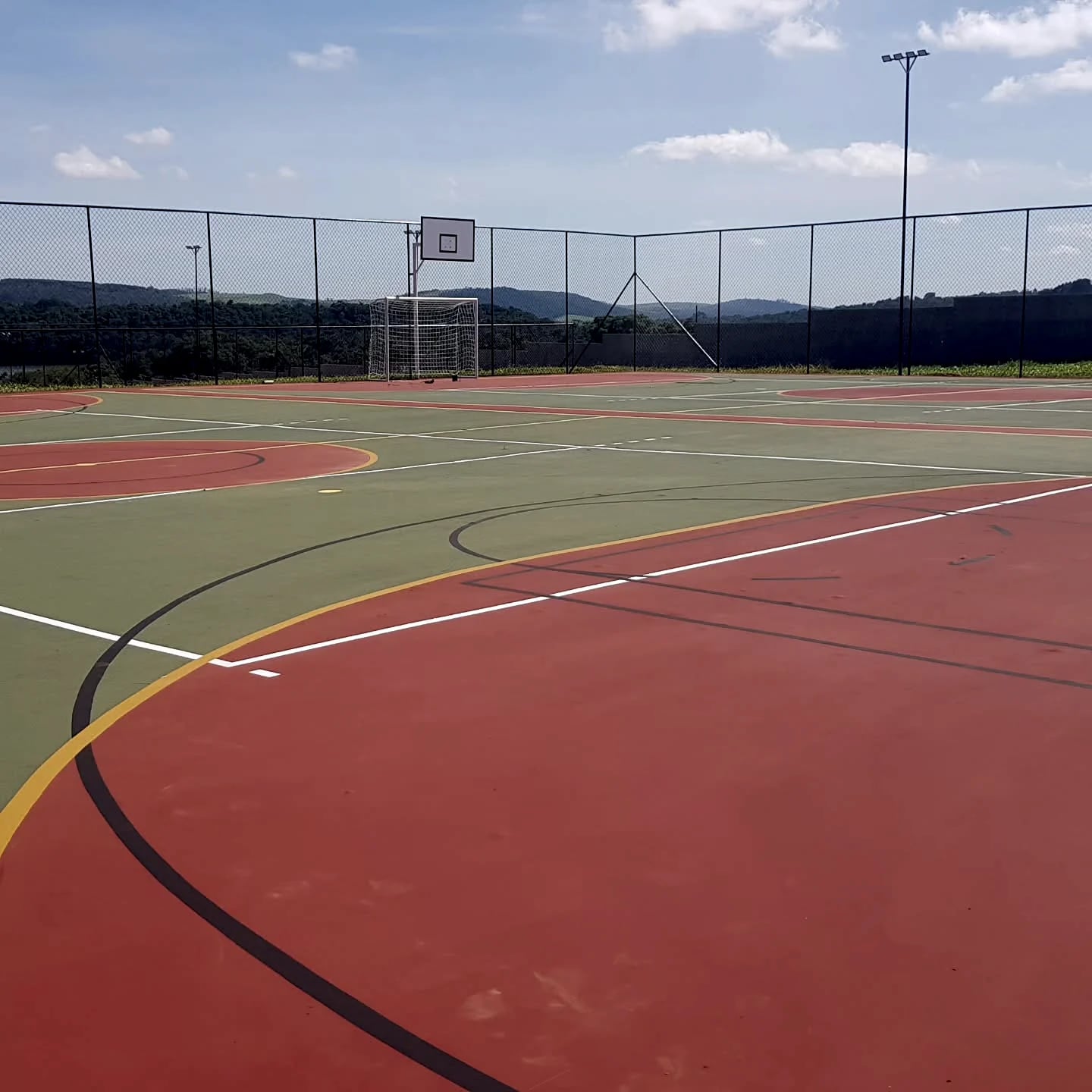 Quadra externa com áreas de piso verde e terracota e marcações esportivas variadas.
