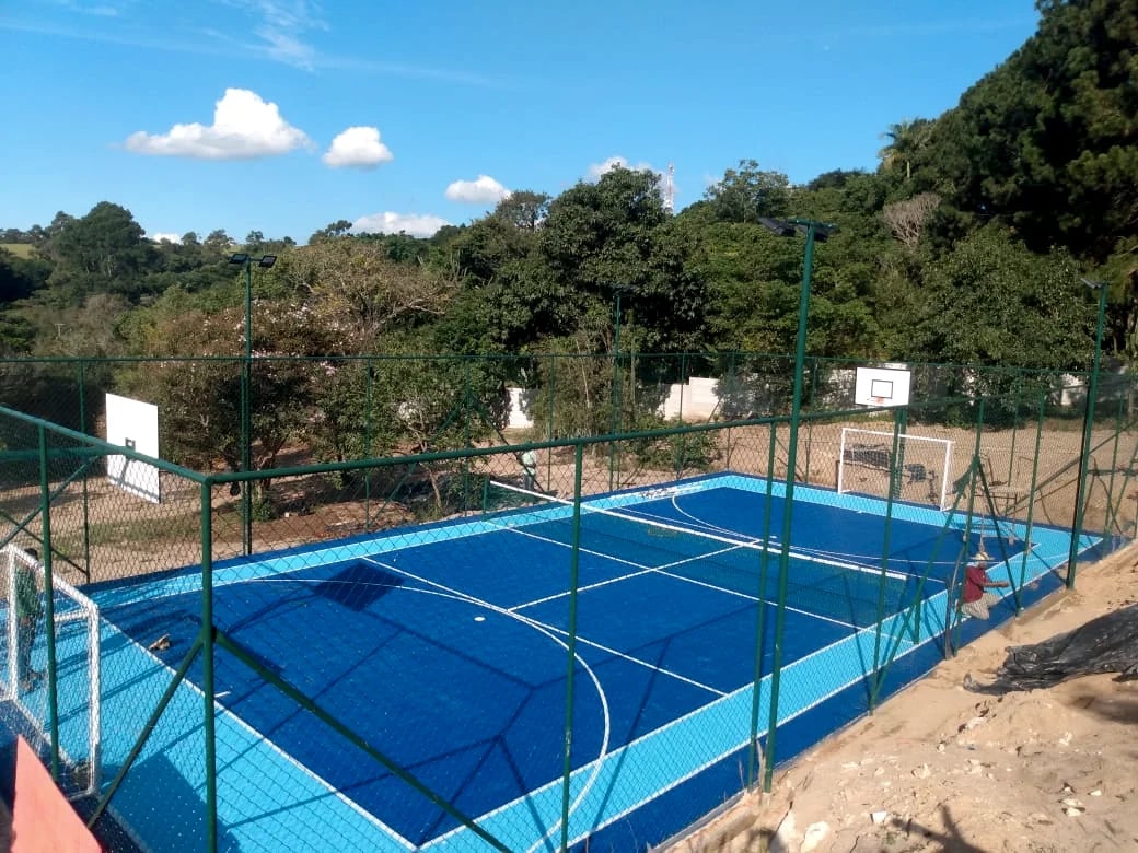 Quadra azul ao ar livre, com alambrado, marcações e tabelas de basquete.